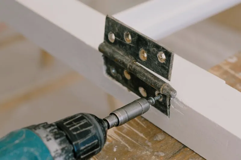 Nail positioned under a door hinge pin ready to be tapped upward with a hammer